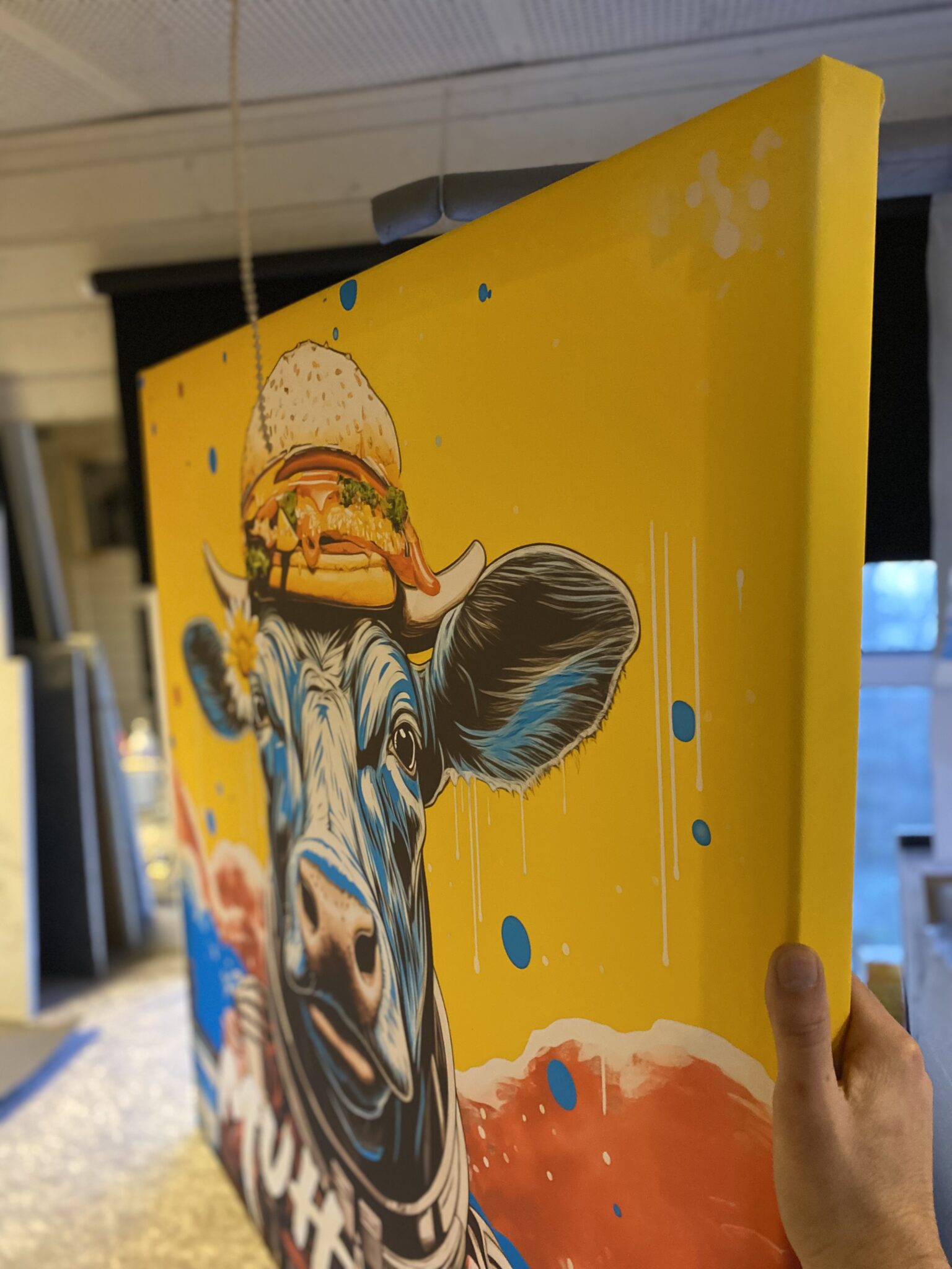 Balthazarts billedkunst, print på lærred som billeder til væggen En person holder en MUH TOO - 100 cm x 100 cm - Kunsttryk på lærred af en ko. Flotte billeder som akustikpanel